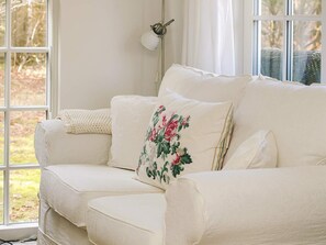 A white sofa with floral pillows and a knitted throw, positioned near a window with curtains. - 4 Star Holiday Home in Vig (Vig)