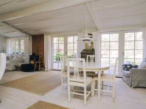A cozy room with a fireplace, a dining table with chairs, and large windows. - 4 Star Holiday Home in Vig (Vig)