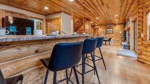 Het interieur van een blokhut met een keuken, inclusief een zwarte koelkast, houten kasten, een granieten aanrecht en zwarte barstoelen.