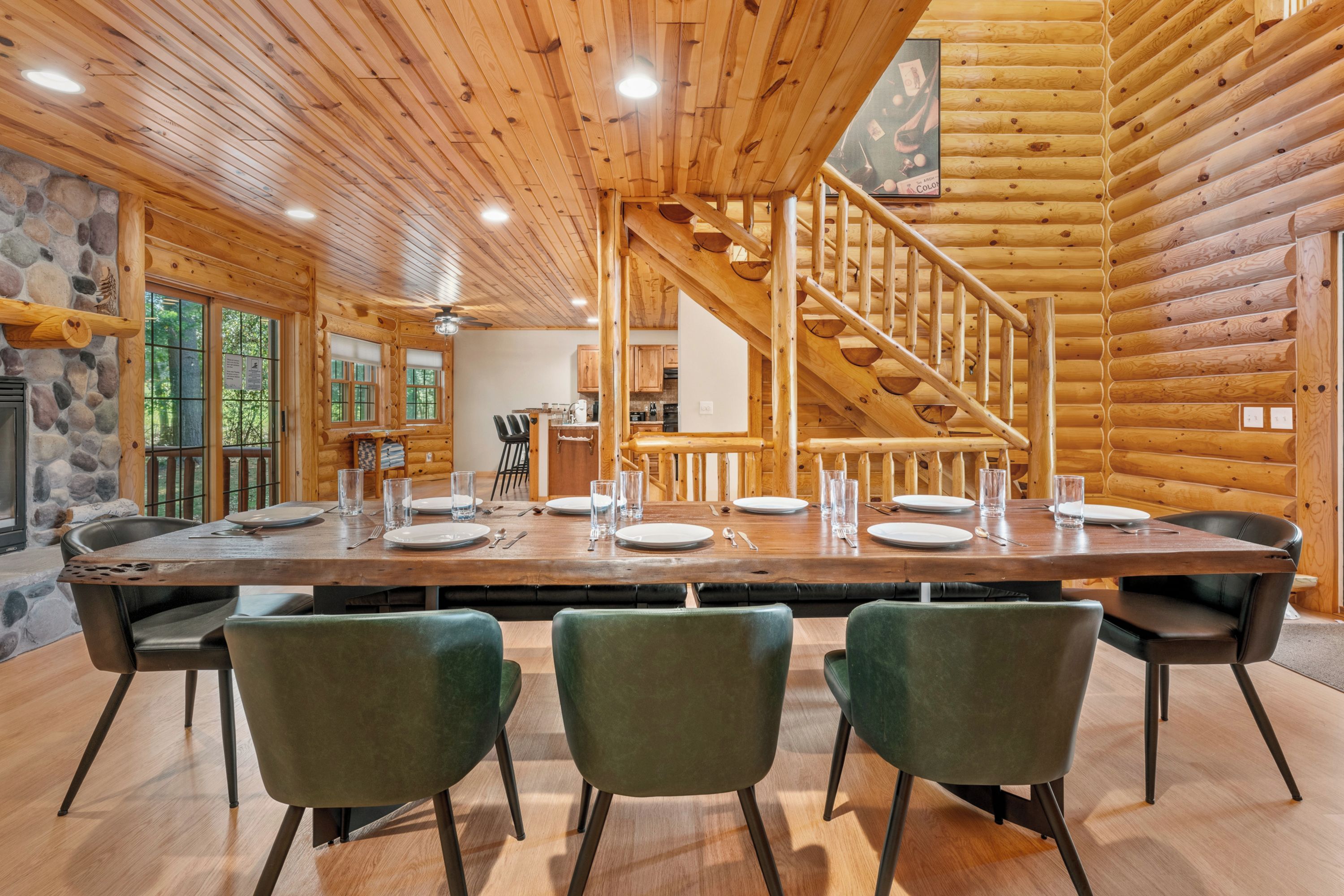 Un interior de madera con una larga mesa de comedor para cuatro, una escalera y una chimenea de piedra.