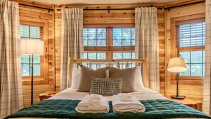 Een slaapkamer in blokhutstijl met een bed, kussens, een groene sprei en twee opgevouwen handdoeken.