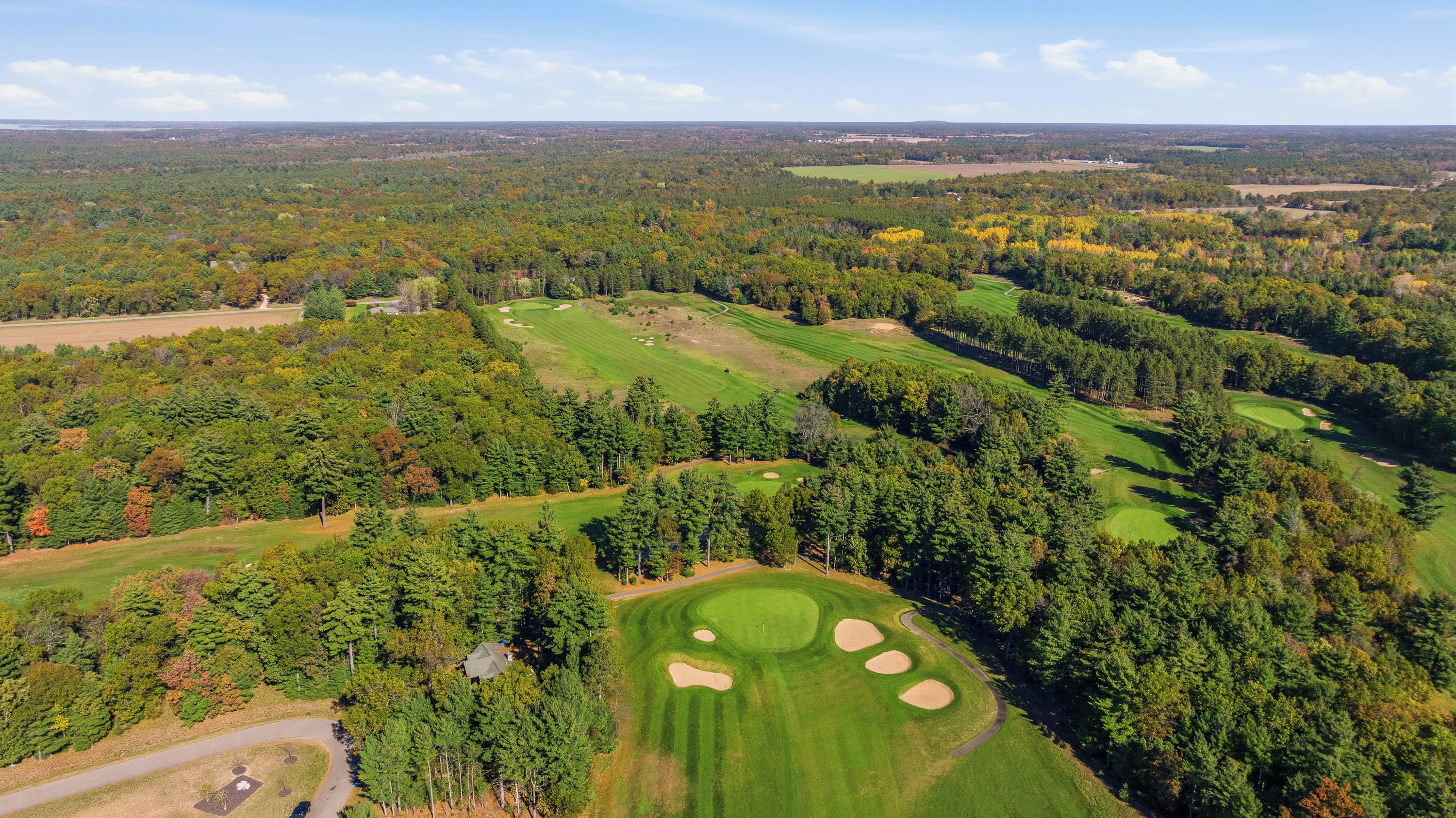Vista aérea de un campo de golf con múltiples greens y bunkers de arena, rodeado de un bosque denso.