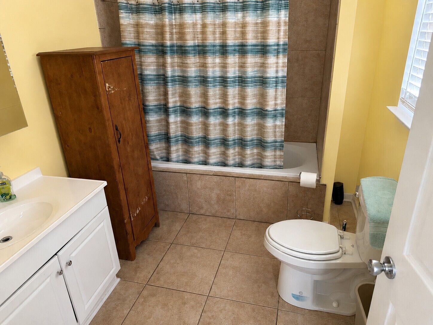 A bathroom with a bathtub, toilet, and wooden cabinet.