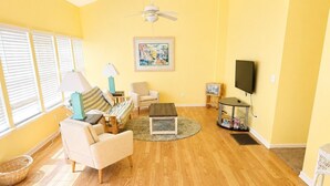 Uma sala de estar com sofá, poltronas, mesa de centro, televisão e ventilador de teto.