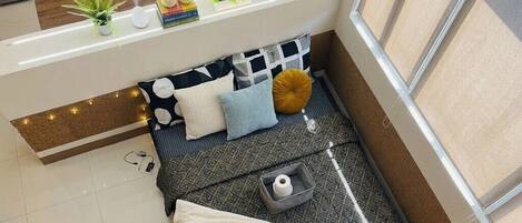 A cozy corner with a cushioned seating area, a small table with a candle, and a shelf with decorative items.