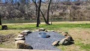 Un parc au bord du lac, équipé d’un foyer, d’une table de pique-nique et entouré d’arbres.