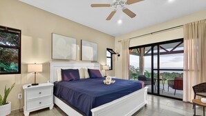 Ein Schlafzimmer mit einem Bett, Nachttischen, einem Deckenventilator, Kunstwerken und einem Balkon mit Gartenmöbeln.