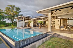 Un espace piscine extérieur moderne doté d’un patio couvert, de chaises longues et d’un coin repas.