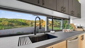 Eine moderne Küche mit großem Fenster, einer schwarzen Spüle und Holzschränken.