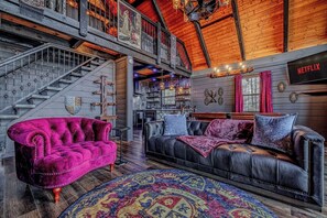Ein geräumiger Loft mit hoher Decke, einer Wendeltreppe, einem Ledersofa, einem farbenfrohen Teppich und einem Netflix-Schild.