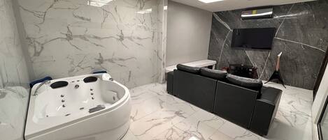 A modern bathroom with a jacuzzi, a black vanity, a flat-screen TV, and a guitar.