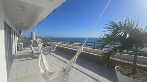 Ein Balkon mit einer Hängematte, Gartenmöbeln, einem Blumentopf und Blick auf das Meer und Gebäude.