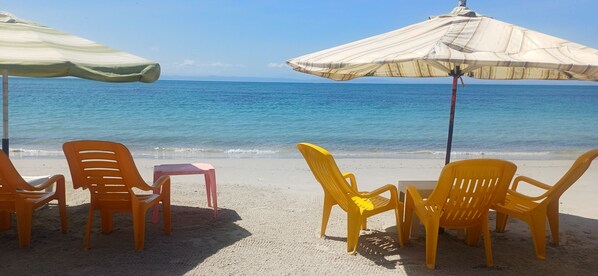 Une plage avec des chaises et des parasols, une table, et l’océan en arrière-plan.