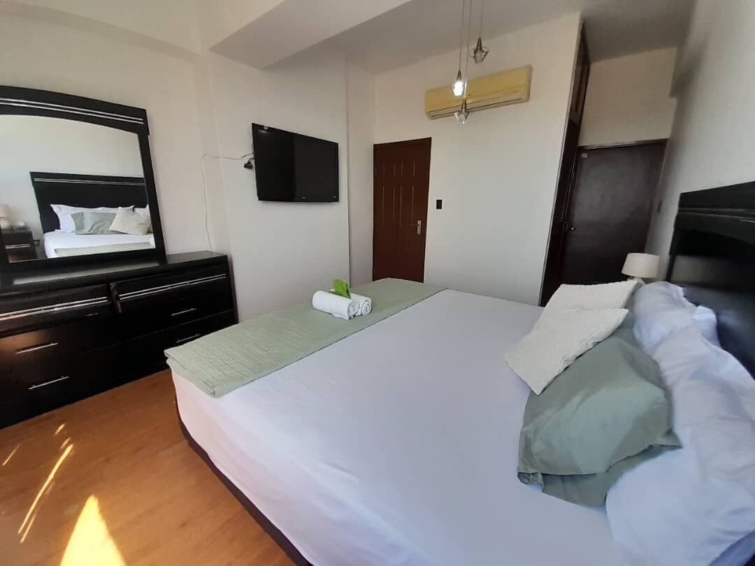 Un dormitorio con cama, cómoda, televisor de pantalla plana, puerta y unidad de aire acondicionado.