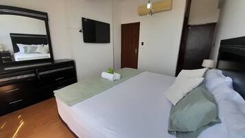 Un dormitorio con cama, cómoda, televisor de pantalla plana, puerta y unidad de aire acondicionado.