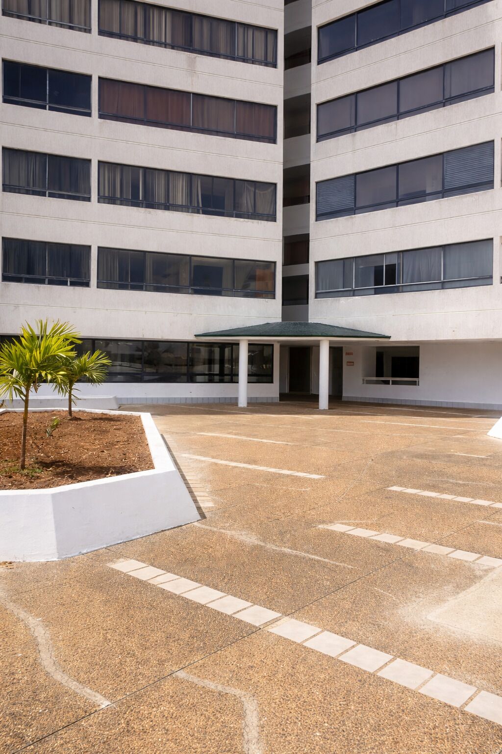 A multi-story building with a covered entrance and a landscaped area with small trees.