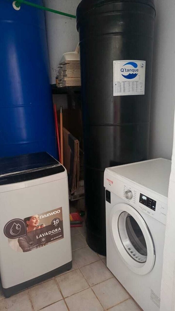 Ein Waschbereich mit Waschmaschine, einem großen schwarzen Wassertank und einem blauen Fass.