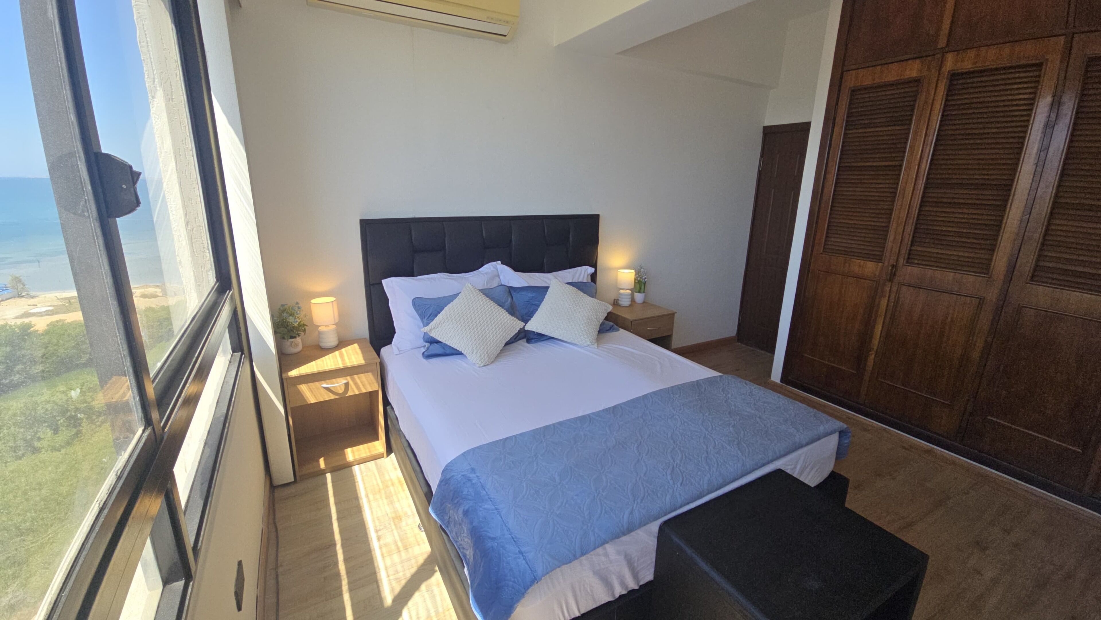 Un dormitorio con cama, mesitas de noche, una ventana y vistas al exterior.