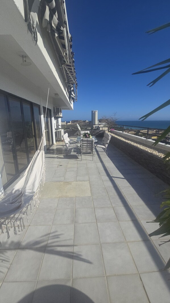 A rooftop terrace with outdoor seating, a view of the sea, and a building with large windows.
