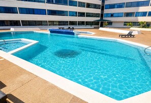 A rectangular pool with clear blue water, surrounded by a tiled deck. There are lounge chairs and a small boat in the pool.