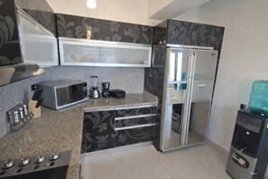 A compact kitchen with a microwave, toaster, blender, and a refrigerator.