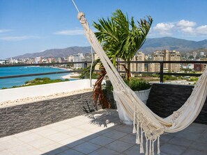 Un hamac sur un balcon donnant sur une plage, avec une vue sur la ville en arrière-plan.