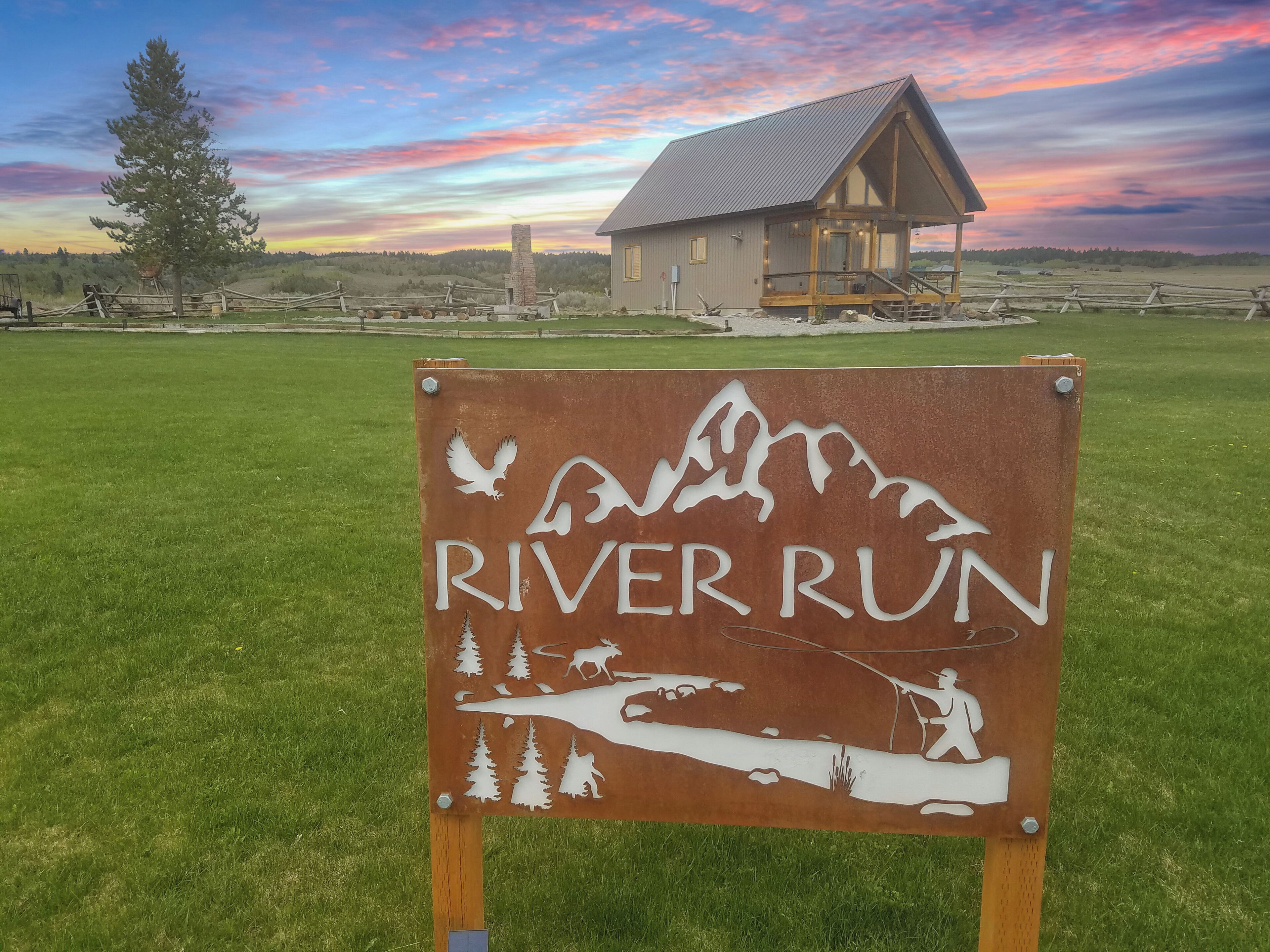 A sign with 'RIVER RUN' and wildlife silhouettes, a wooden cabin, and a grassy field.