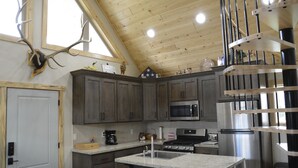 A kitchen with wooden cabinets, a stainless steel refrigerator, a microwave, and a sink. - The River Run Cabin (Ashton)