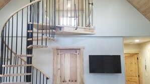 A loft-style room with a wooden staircase, a flat-screen TV mounted on the wall, and a small table with a tray. - The River Run Cabin (Ashton)