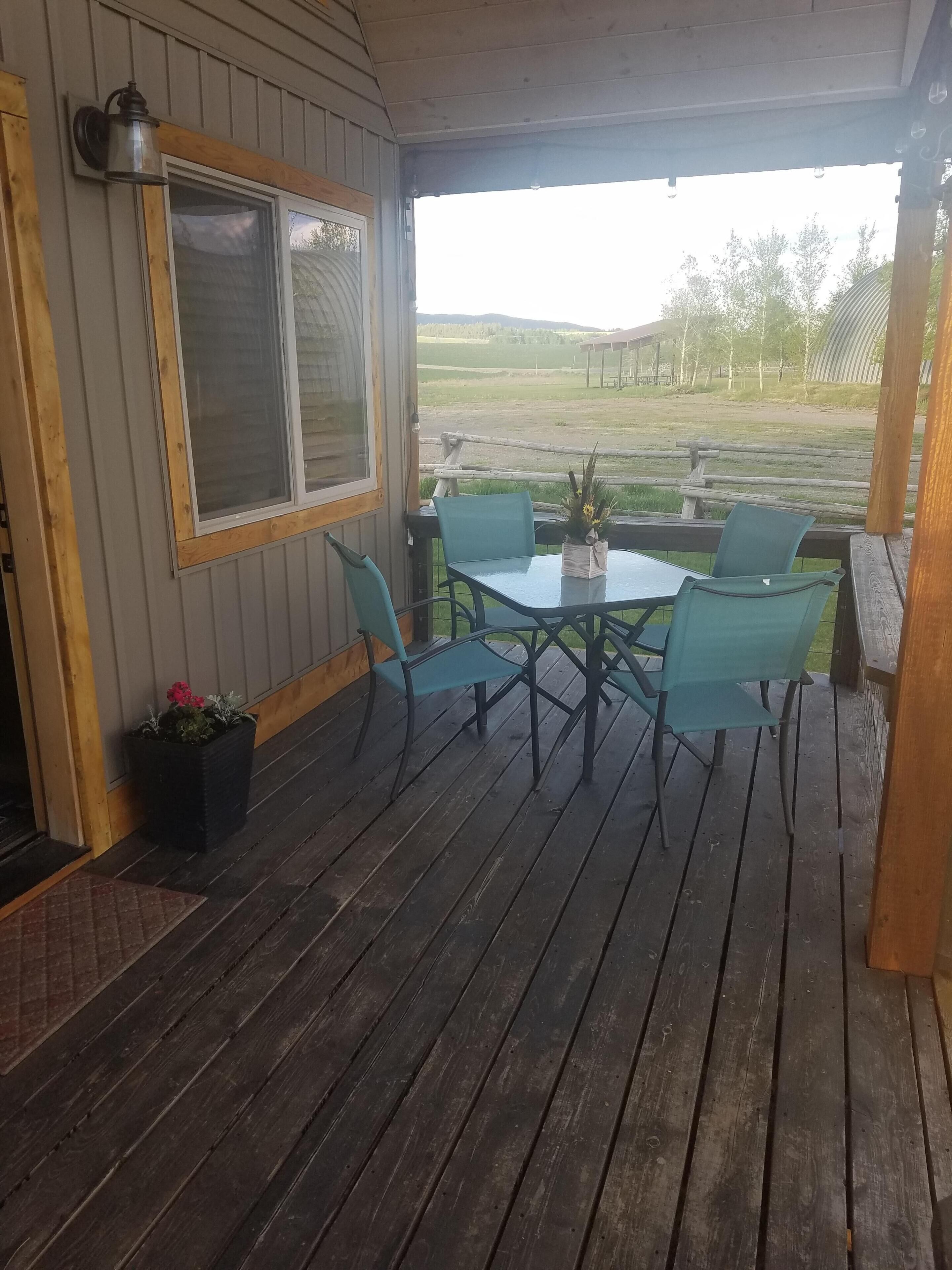 A wooden deck with a table and chairs, a potted plant, and a view of a grassy field.