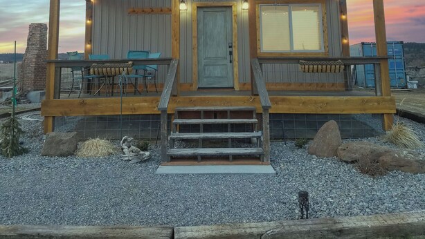 A wooden cabin with a porch, a stone chimney, and a gravel driveway. - The River Run Cabin (Ashton)