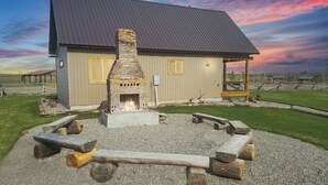 A building with a stone fireplace, a wooden deck, and a gravel area with benches. - The River Run Cabin (Ashton)