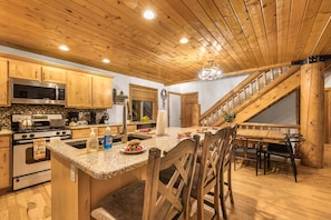 A kitchen with wooden cabinets, a granite countertop, a stainless steel microwave, and a wooden staircase.