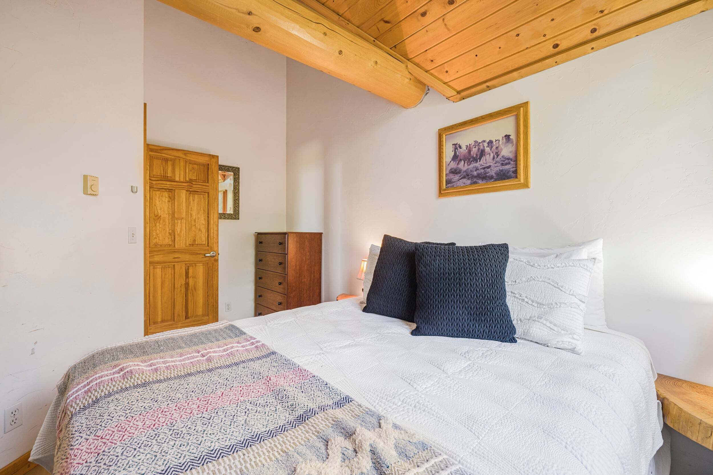 Ein Schlafzimmer mit Holzboden, einem Bett mit gemustertem Überwurf, einem Holzschrank und einem gerahmten Bild an der Wand.