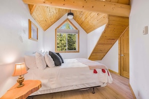 A bedroom with a sloped ceiling, a bed with pillows, a bedside table with a lamp, and a window.
