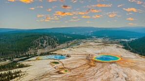 Un vaste paysage dominé par une importante zone géothermique, avec de magnifiques sources chaudes aux couleurs vives, entourée de forêts denses et de montagnes lointaines.