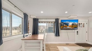 Un soggiorno moderno con zona pranzo, ampie finestre, una TV a schermo piatto e vista su un paesaggio montuoso.