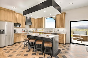 A modern kitchen with wooden cabinets, a large island with stools, a stainless steel refrigerator, and a view of a patio.