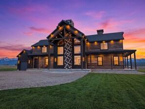 A large, modern house with a prominent central tower, multiple windows, and a well-maintained lawn. - Checkmate (Island Park)