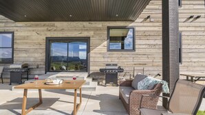 An outdoor patio with a wooden table, wicker furniture, and a grill. - Checkmate (Island Park)