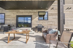 An outdoor patio with a wooden table, wicker furniture, and a grill. - Checkmate (Island Park)