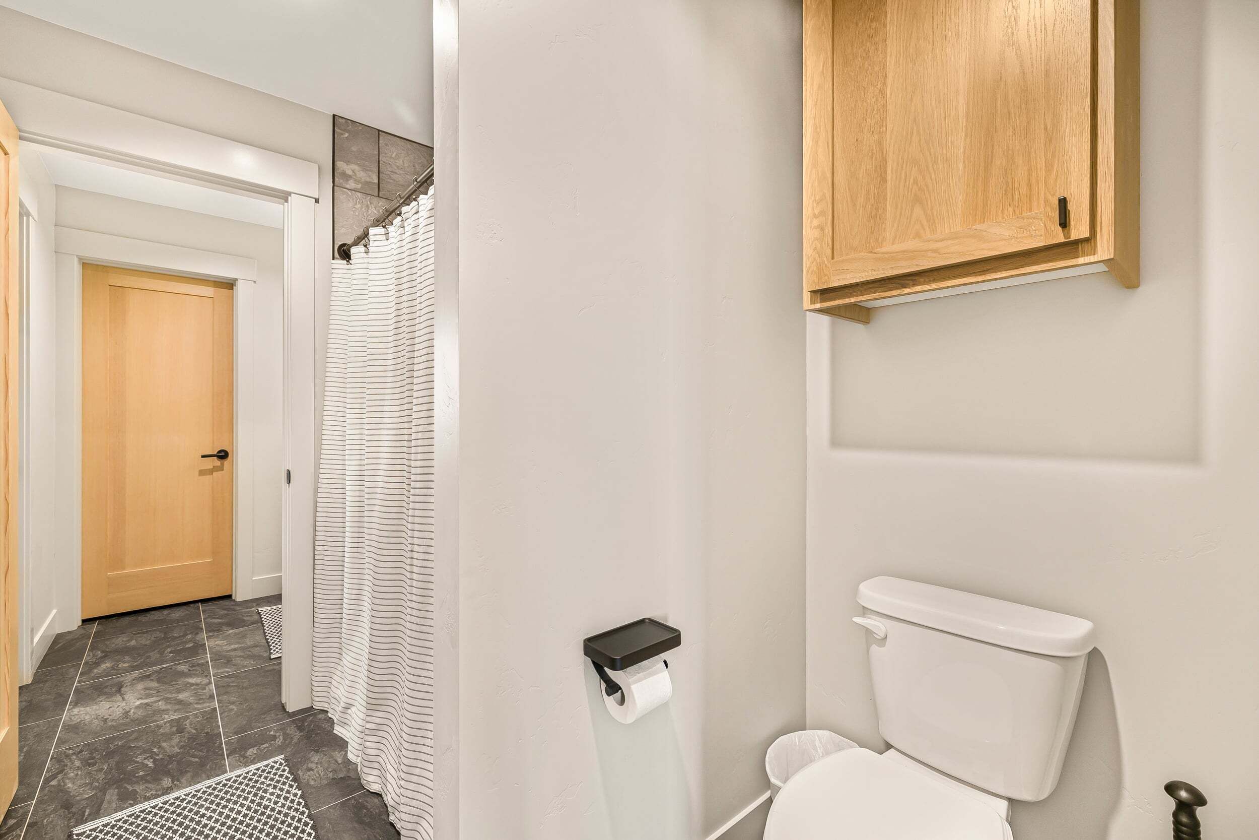 Une salle de bain avec des toilettes, un rideau de douche et un meuble en bois.