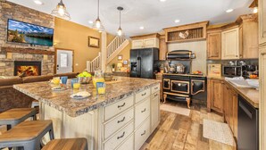 A kitchen with a large island, wooden cabinets, a built-in oven, and a stone fireplace. - Jensen Pines (Island Park)