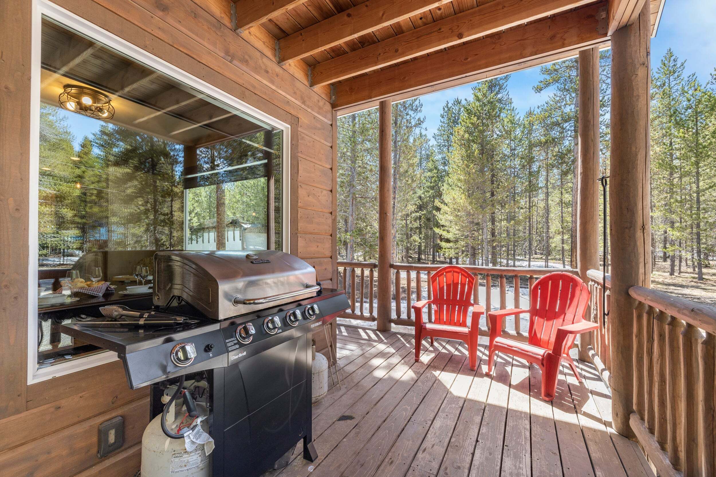 A wooden deck with a grill, chairs, and a view of a forest.