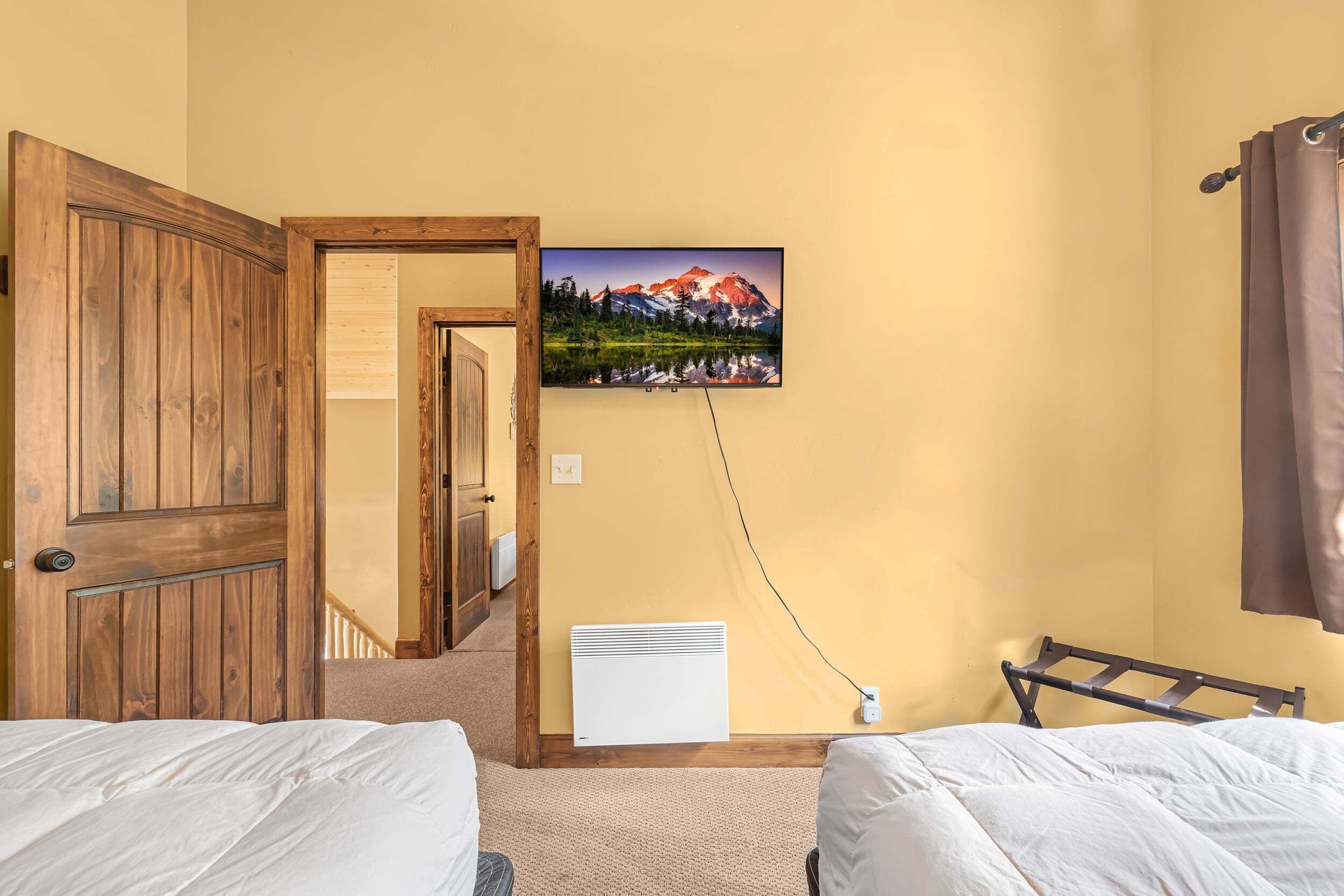 Une chambre d’hôtel avec deux lits, une porte en bois, un tableau représentant un paysage de montagne et un radiateur blanc.