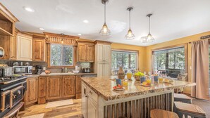 A kitchen with wooden cabinets, a granite island, bar stools, and pendant lighting. - Jensen Pines (Island Park)