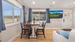 Ein Essbereich mit Tisch und Stühlen, einem Fernseher an der Wand und Blick ins Freie.
