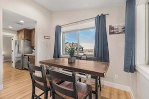 A modern kitchen with a dining area, wooden cabinets, a stainless steel refrigerator, and a window with curtains. - Victor Traverse (Victor)