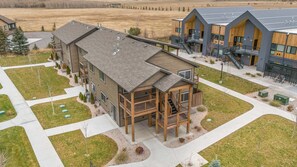 Un bâtiment moderne à plusieurs étages, doté d’une terrasse en bois, d’un espace extérieur couvert et d’un parking.