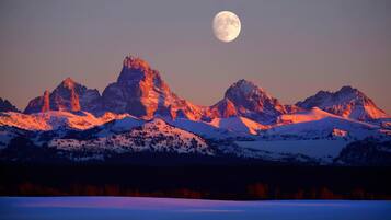 Paisaje montañoso con picos nevados y una luna llena en el cielo.